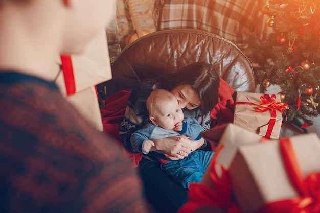 Free photo woman sitting on a sofa with a baby in her arms and with a mountain of brown gifts with red bow