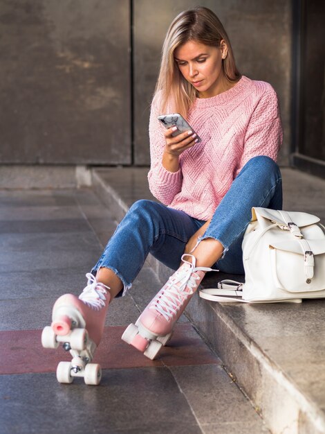 Woman sitting on stairs with roller skates and looking at smartphone