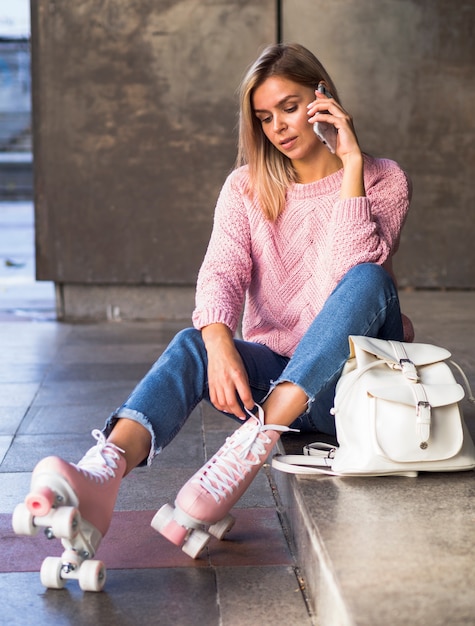 Free photo woman sitting on stairs with roller skates and smartphone