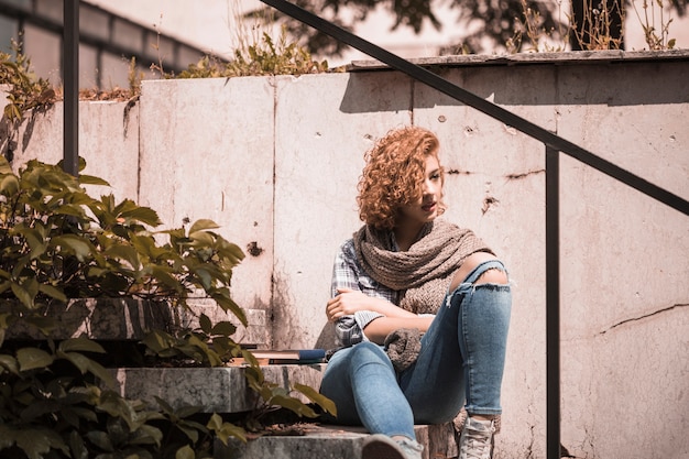 Free photo woman sitting on steps near books in public garden