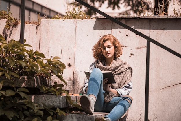 Free photo woman sitting on steps and reading book