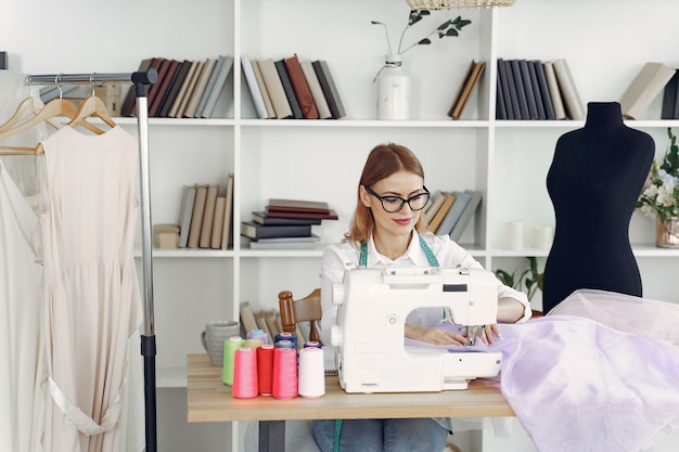 Free photo woman sitting in studio and sew cloth