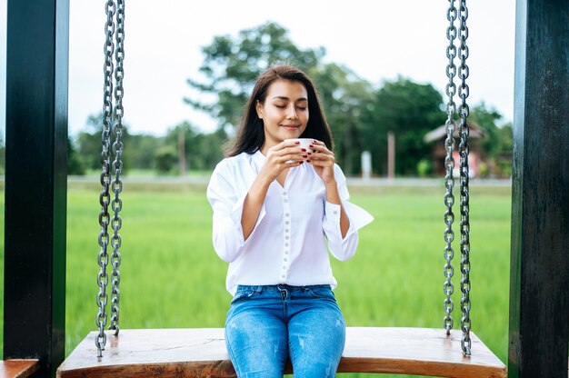 Woman sitting on a swing and holding a cup of coffee