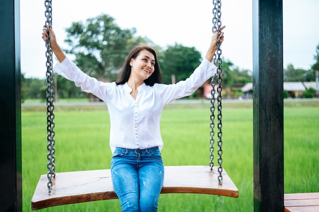 Free Photo woman sitting on a swing and holding her hand at the chain