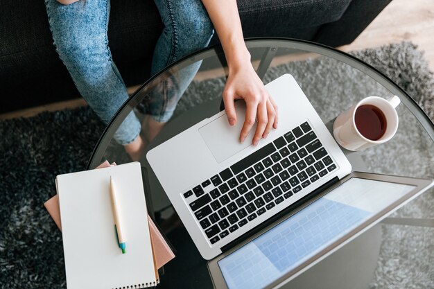 Woman sitting and using laptop on glass table at home