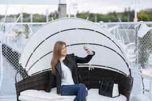 Free photo woman sitting in a wicker armchair doing an auto photo