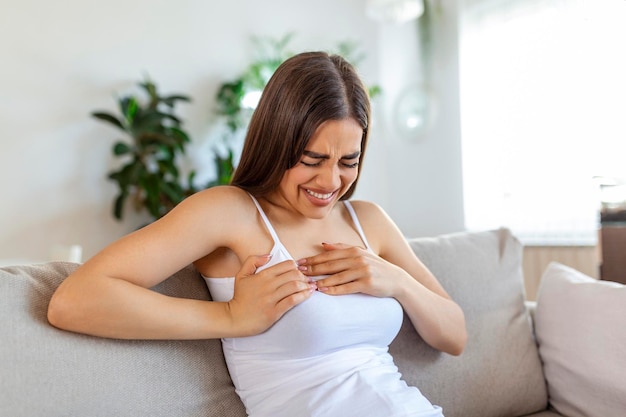 Woman sitting with strong chest pain and hands touching her chest while having trouble at home Heart attack or heart failure symptom