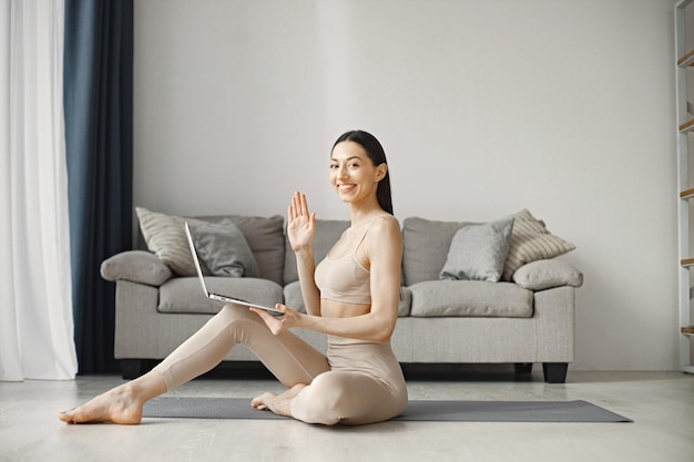 Woman sitting on yoga man in leggins and top while using on laptop at home