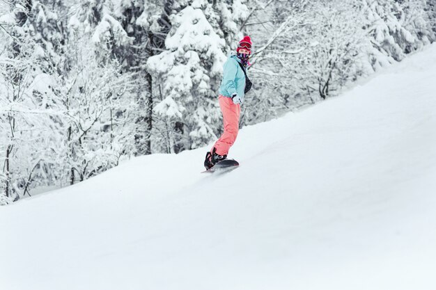 Woman in ski suit looks over her shoulder going down the hill on her snowboard 