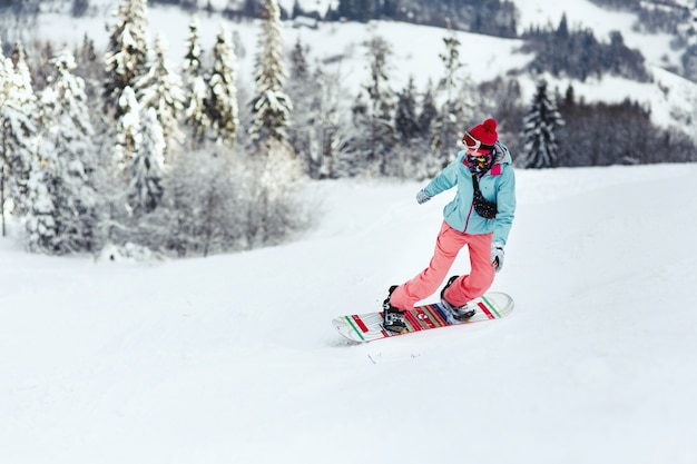 Free photo woman in ski suit looks over her shoulder going down the hill on her snowboard