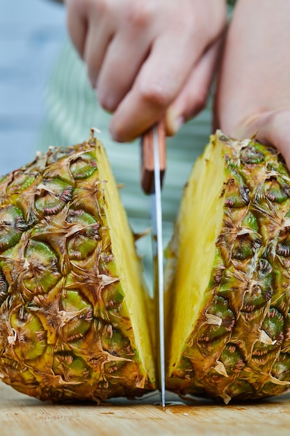 Woman slicing a fresh pineapple on a wooden cutting board, close up