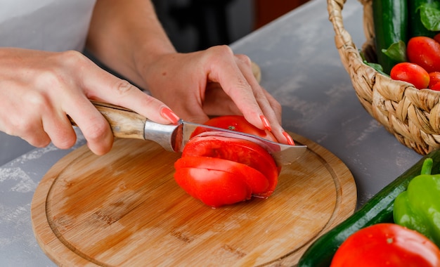 Free photo woman slicing tomato on a cutting board high angle view on a gray surface