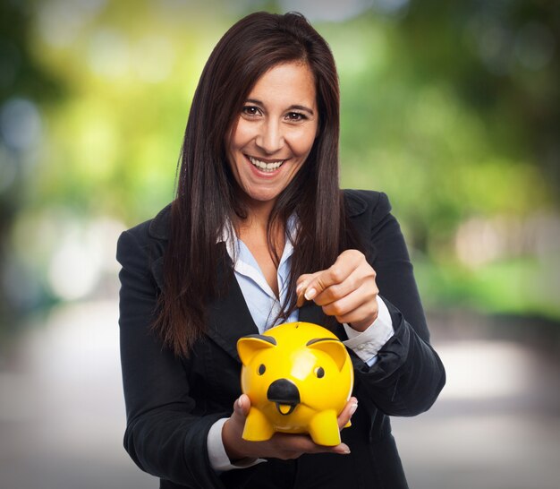 Woman smiling in suit and throwing a coin into a piggy bank