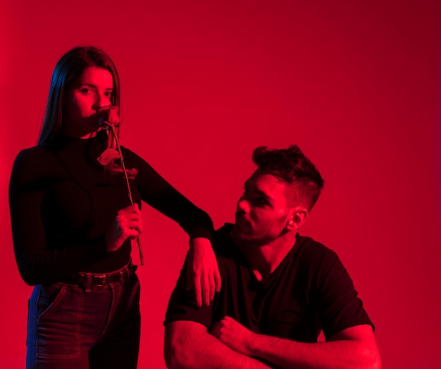 Woman sniffing rose near sitting man 