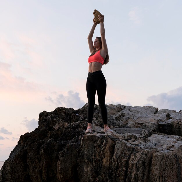 Woman in sportswear standing on a coast with her arms up