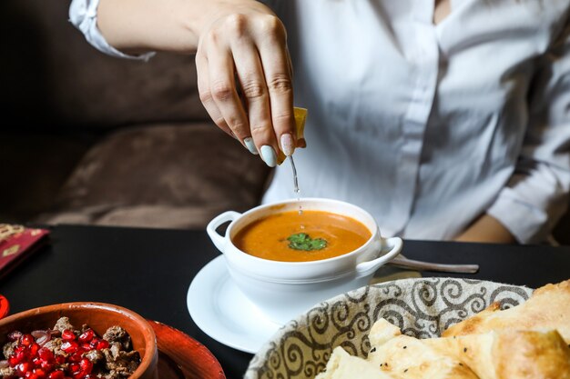 Woman squeeze lemon into lentil soup side view