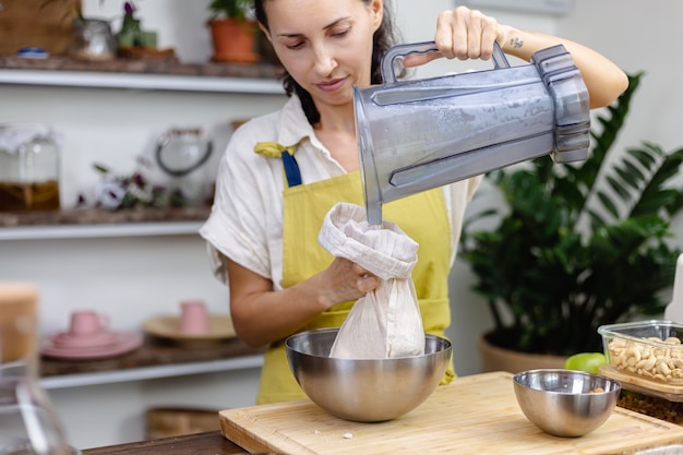 Woman squeezing almond milk from almond in kitchen at home