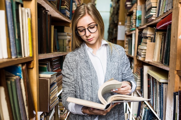 Free Photo woman standing between bookcases and turning book pages