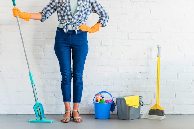 Free photo woman standing in front of brick wall with cleaning equipments