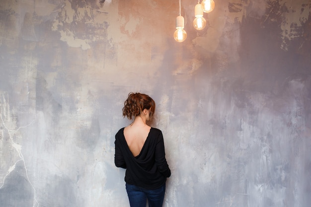 Free photo woman standing in front of grungy concrete back to camera.