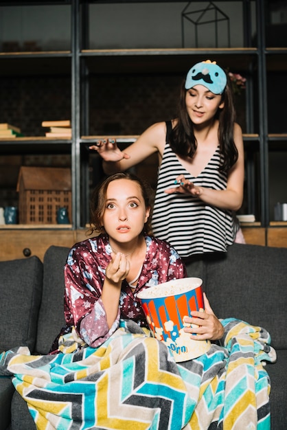 Woman standing behind her friend watching television