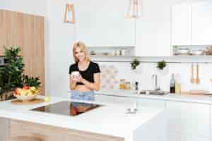 Free photo woman standing on the kitchen with warm cup of coffee