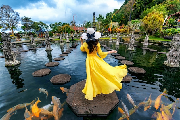 Woman standing in pond with colorful fish at Tirta Gangga Water Palace in Bali, Indonesia