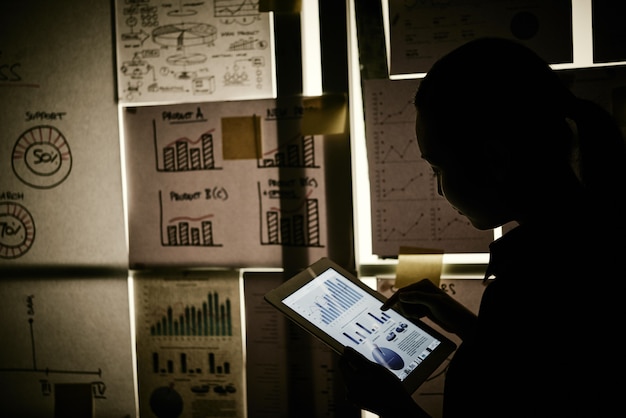 Free photo woman standing next to window covered with business charts and working on tablet