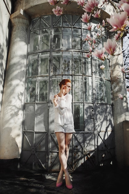 Free photo woman stands near a building and a blossom magnolia