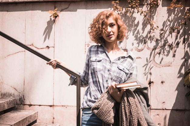 Free photo woman in street wear with books and scarf in hand holding rail