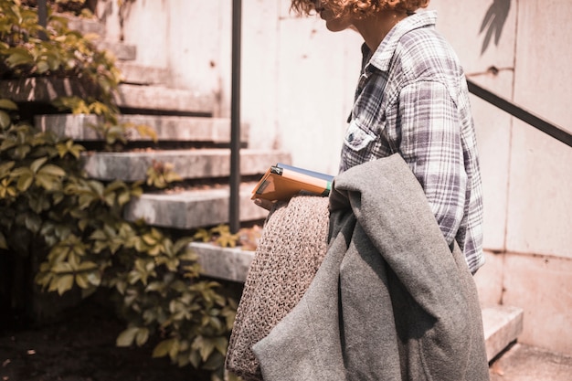 Free photo woman in street wear with books and scarf in hand near steps