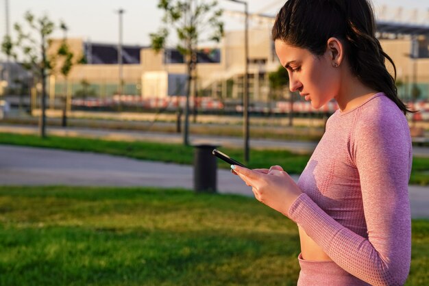 A woman in a suit for yoga does early in the morning with a phone in her hands at dawn.