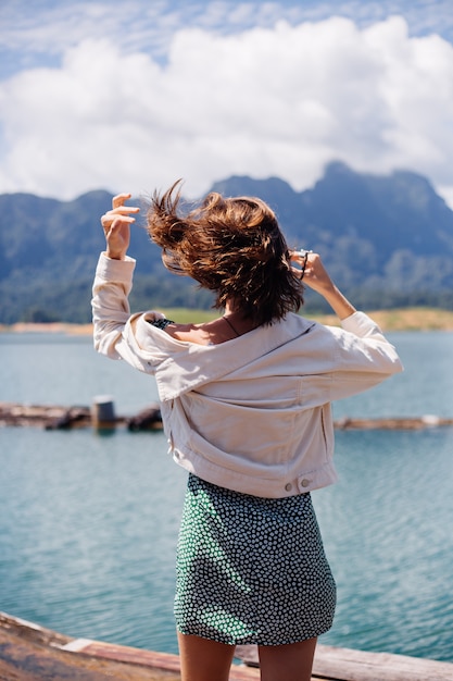 Woman in summer dress and jacket tourist travel in Thailand, Khao Sok national park, amazing view on boats and lake.