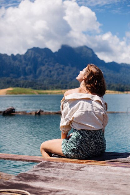 Woman in summer dress and jacket tourist travel in Thailand, Khao Sok national park, amazing view on boats and lake.