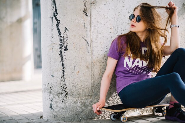 Woman in sunglasses sitting on skateboard