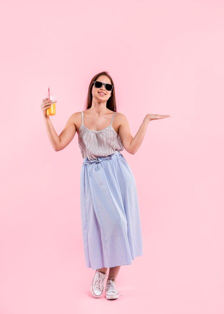 Woman in sunglasses standing and holding glass of juice 