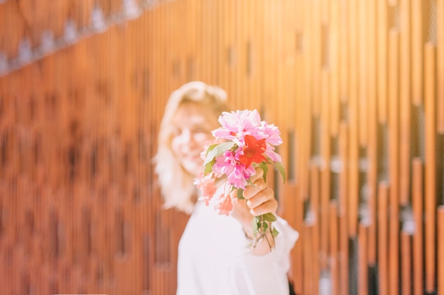 Woman in sunlight showing flowers toward camera