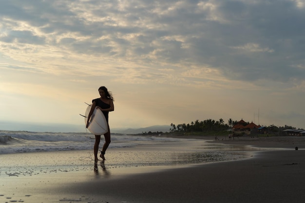 Woman surfer with surfboard on the ocean at sunset