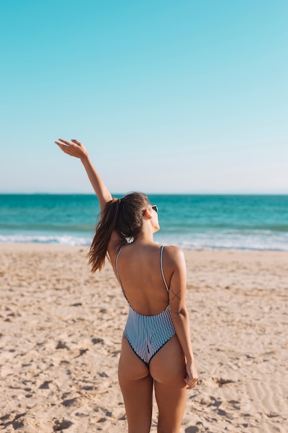 Woman in swimsuit waving hand on seaside