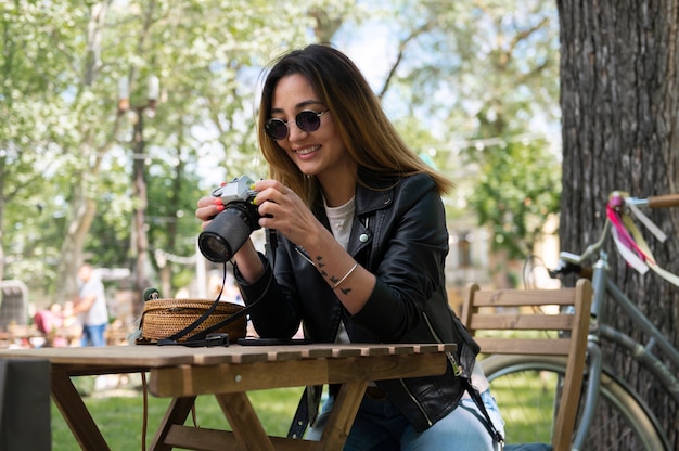 Woman in synthetic leather jacket using camera while outdoors