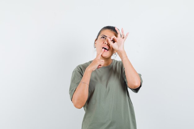 woman in t-shirt showing ok sign on eye and looking pensive