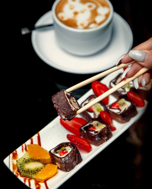 Woman taking chocolate crepe rolls with strawberry banana and kiwifruit with chopsticks