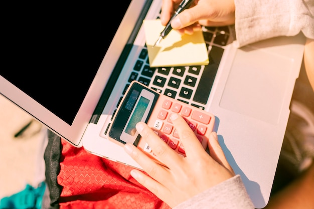 Woman taking notes by hand on laptop in sunny day