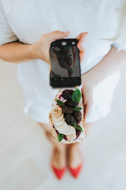 Free photo woman taking a photo of a toast with blackberry jam and vegan cream cheese