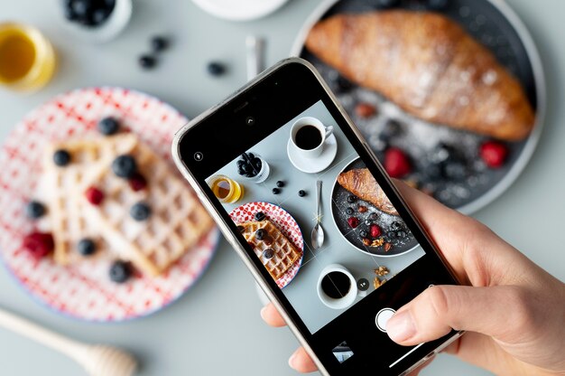 Woman taking photo of waffles and a croissant with fruits