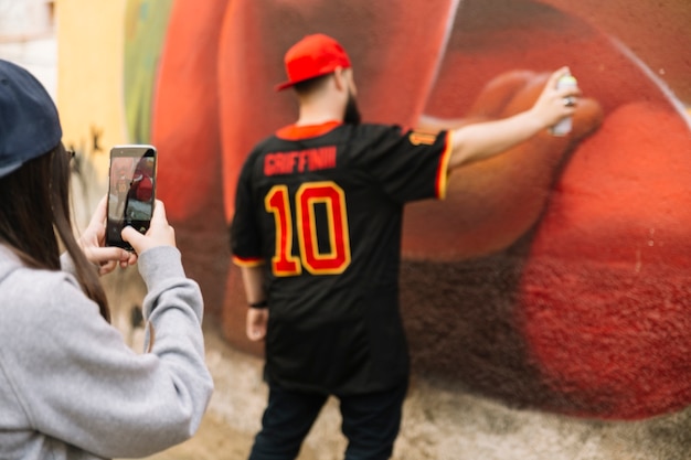 Woman taking photograph of man spraying on graffiti wall