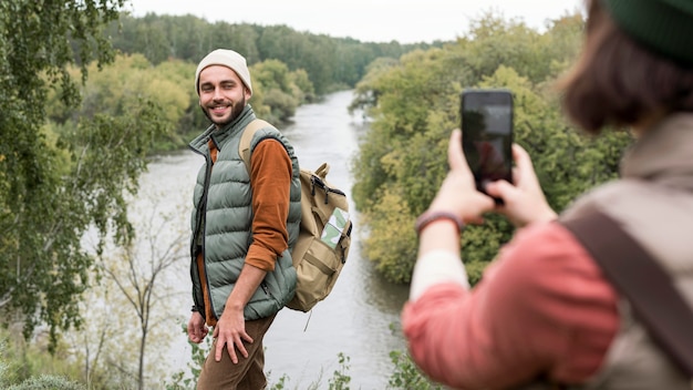 Free Photo woman taking photos of boyfriend in nature with smartphone