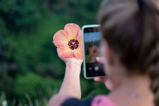 Woman taking a picture with her mobile phone of a flower she is holding in her hand