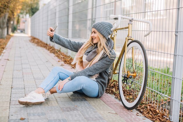 Woman taking selfie near bicycle and fence