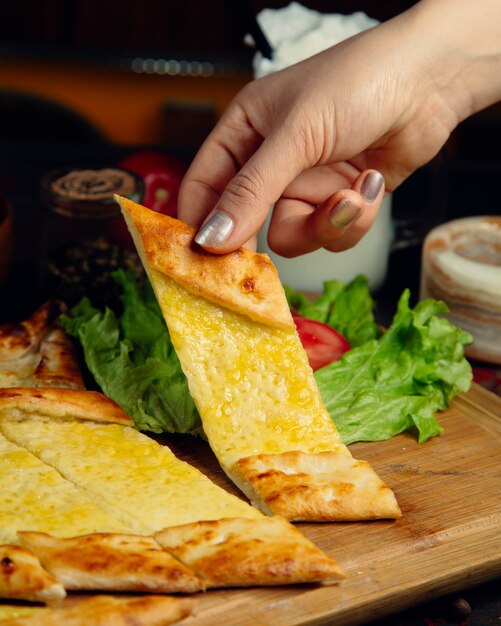 Woman taking a slice of turkish pide bread with melted cheese.